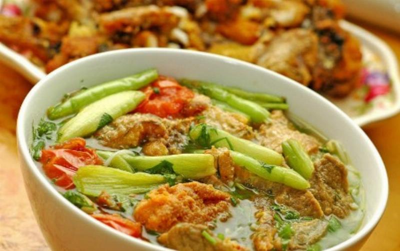Một đĩa chả cá anh vũ chiên vàng giòn, đặt trên đĩa với bún tươi, rau sống và chén nước chấm chua ngọt, thể hiện cách thưởng thức món ăn hấp dẫn
